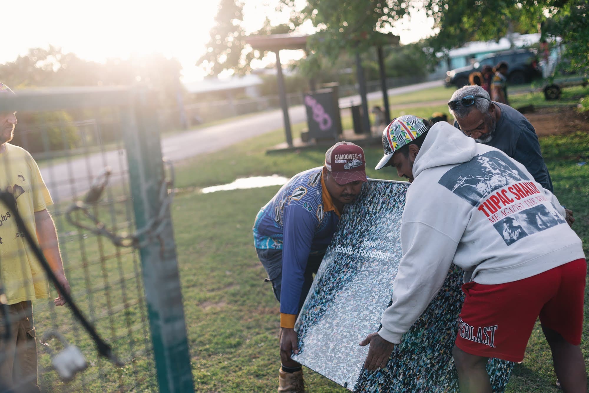 Community members on Palm Island carrying a pressed recycled-plastic panel marked Goods x Snow Foundation
