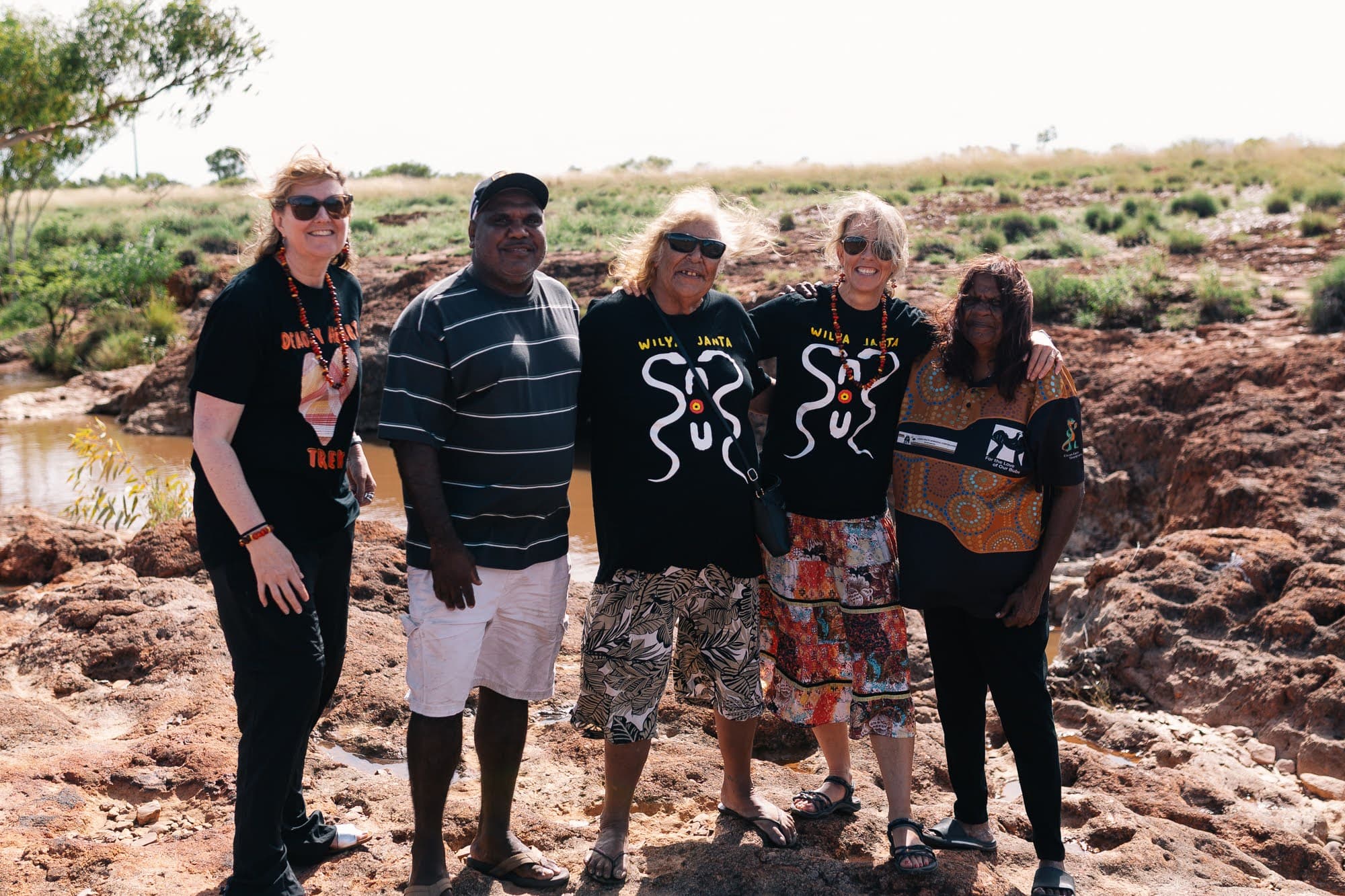 Sally Grimsley-Ballard, Jimmy Frank Jupurrurla, Linda Turner, Georgina Byron AM and Patricia Frank standing together on rock beside a waterhole at Tennant Creek