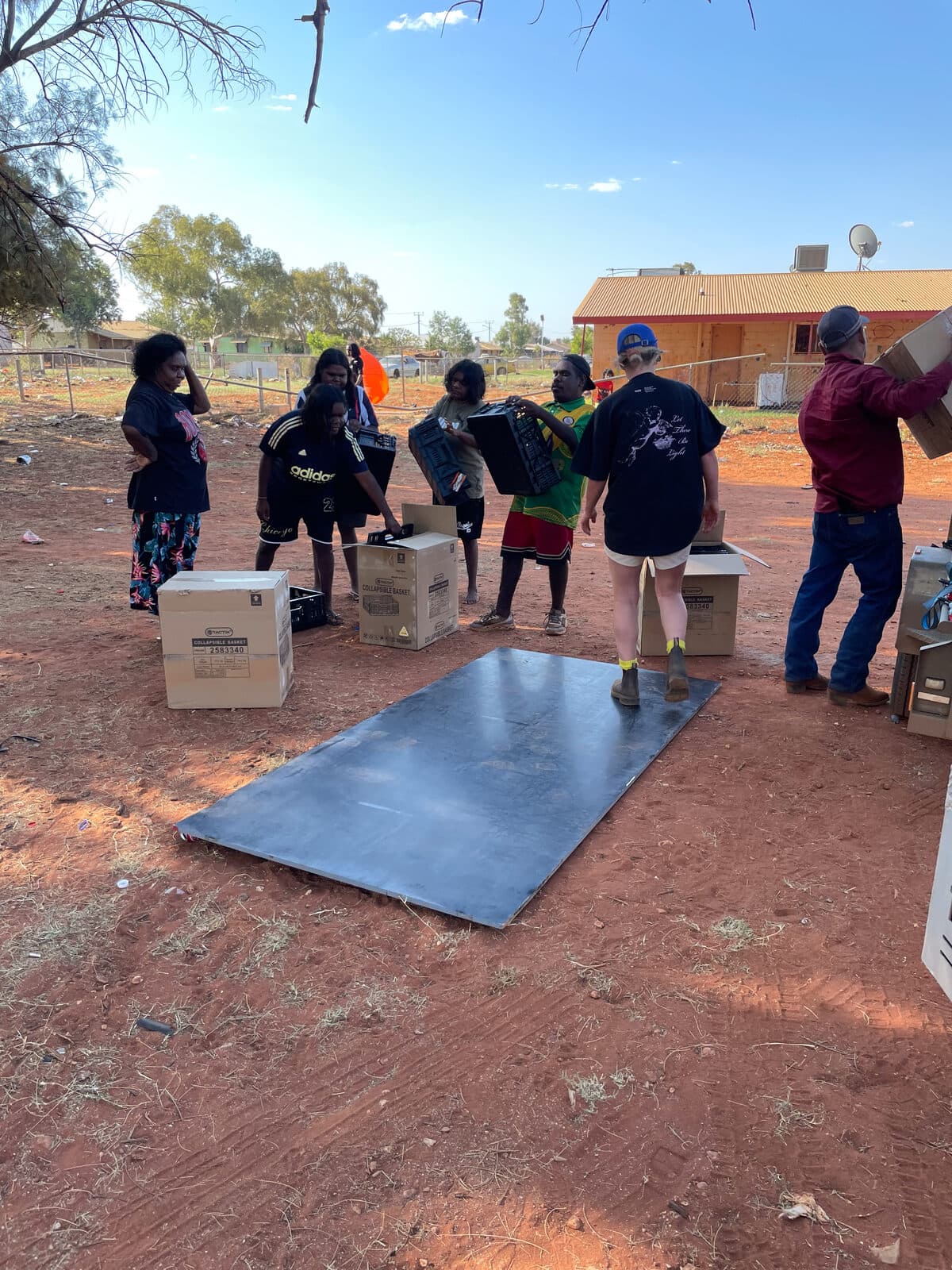 Community members unpacking black recycled plastic bed parts on red dirt