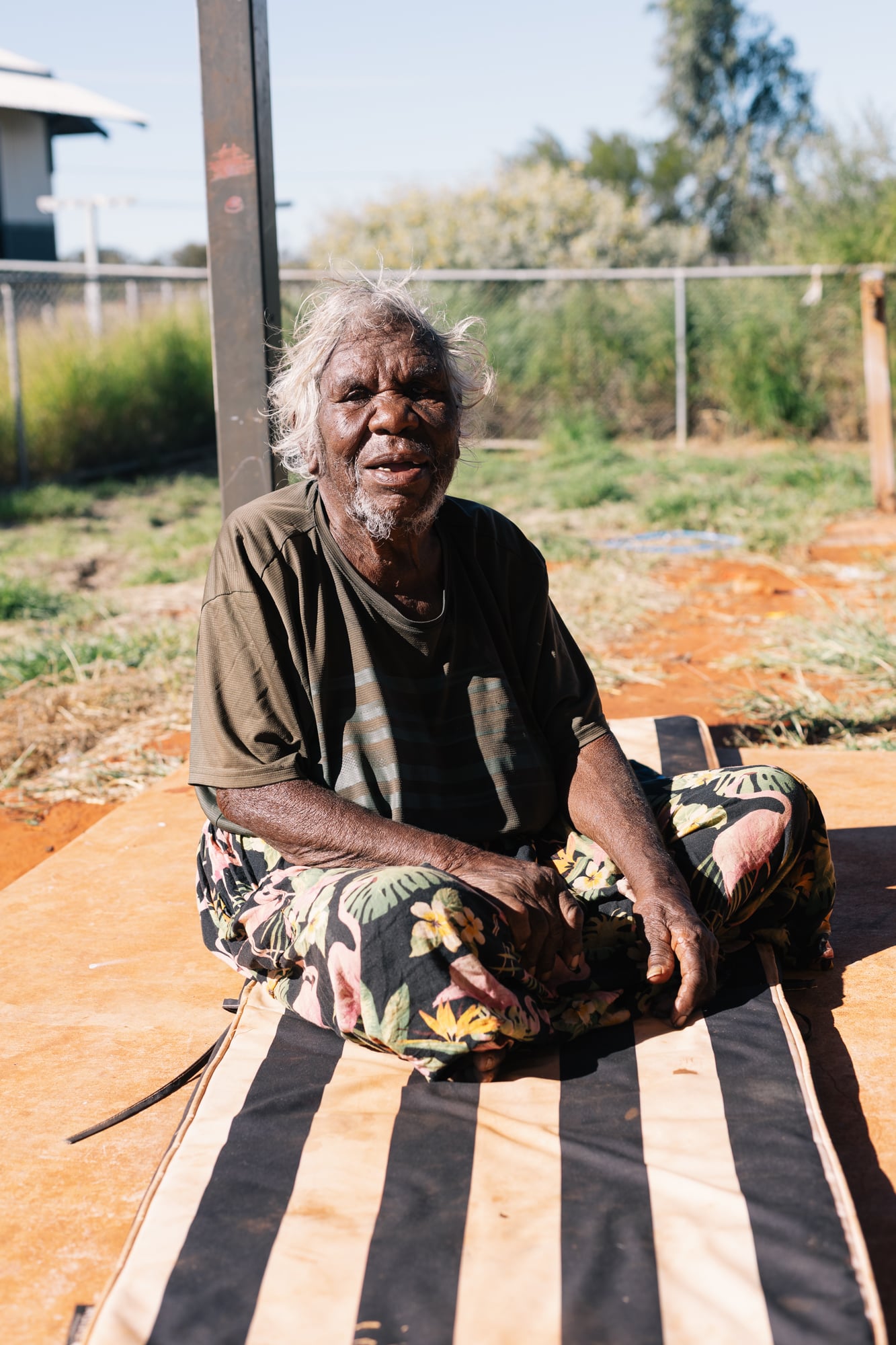 A household member sitting on a thin mattress on the ground.